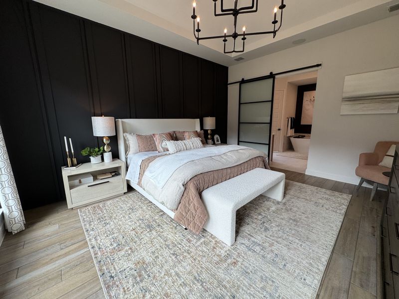 A stylish bedroom featuring a dark accent wall, elegant chandelier, and sliding door leading to a modern bathroom.