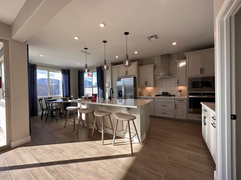 A spacious kitchen with sleek white cabinets, a central island, pendant lighting, and woodgrain tile flooring.