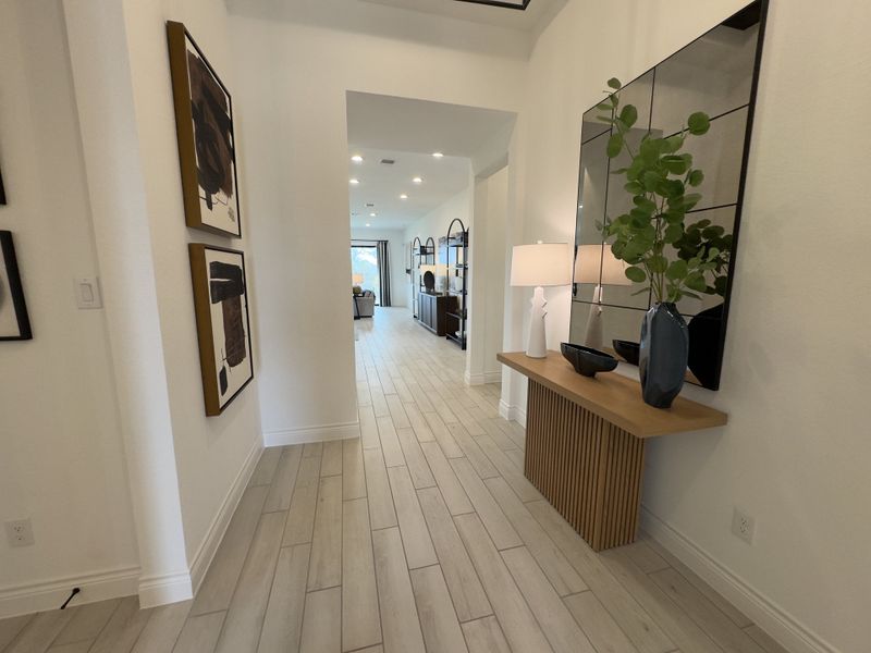 A modern hallway with light wood flooring, chic wall art, and a stylish console table adorned with plants and decor.