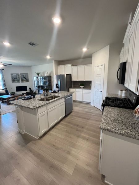 A modern kitchen with white cabinets, granite countertops, and wood flooring, seamlessly flowing into a cozy living area.