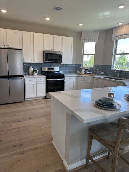 A modern kitchen featuring white cabinetry, a sleek island, stainless appliances, and light wood flooring.