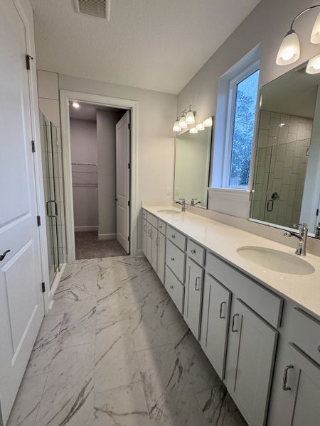 Elegant bathroom featuring a spacious vanity, marble-style floors, and modern lighting.