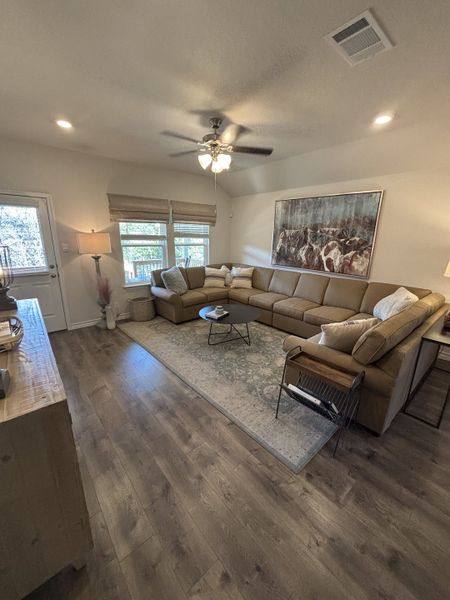 A cozy living room featuring a large sectional sofa, hardwood floors, artistic decor, and natural light from large windows.