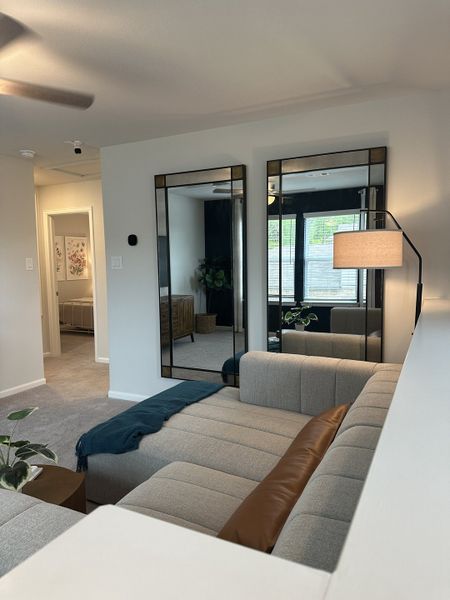 A cozy living room with modern mirrors, a plush sectional, floor lamp, and soft carpeting. Perfect for relaxing and entertaining. A cozy living room with modern mirrors, a plush sectional, floor lamp, and soft carpeting. Perfect for relaxing and entertaining.