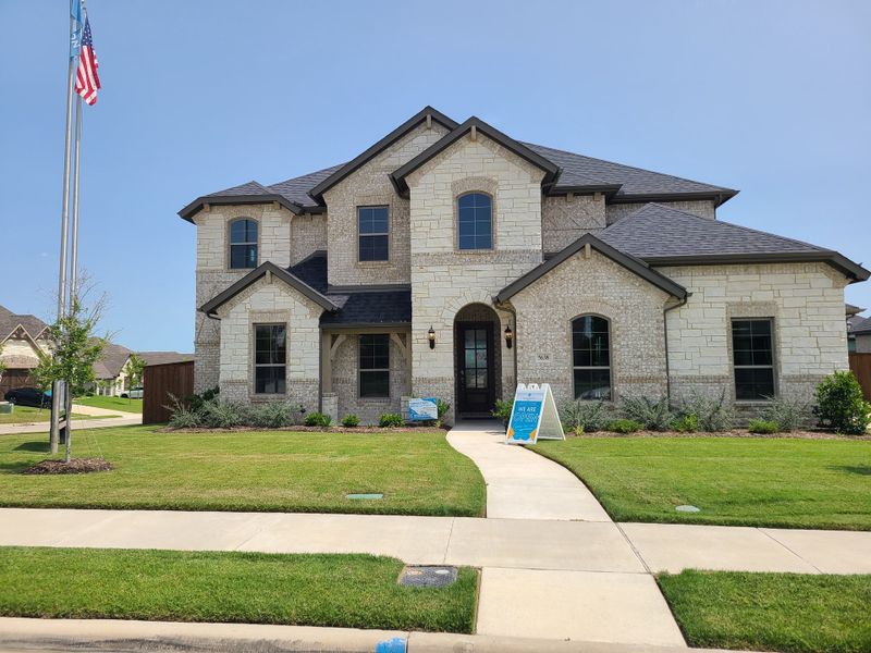 A beautiful stone and brick home with manicured lawn in Hayes Crossing Phase 2 by John Houston Homes (Midlothian, TX).