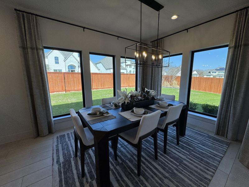 A chic dining room with a dark wood table, white chairs, and large windows overlooking a lush backyard.