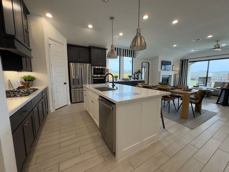 A modern kitchen with sleek dark cabinets, a spacious island, and stainless steel appliances, flowing into an elegant dining area.