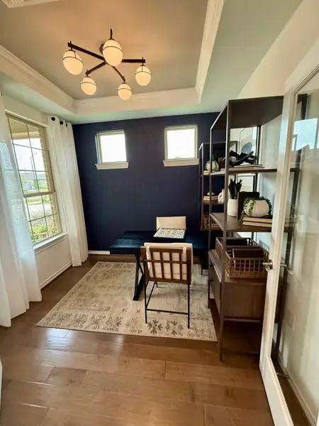 A cozy study with rich wood floors, a modern chandelier, navy accent wall, and ample natural light from large windows. A cozy study with rich wood floors, a modern chandelier, navy accent wall, and ample natural light from large windows.