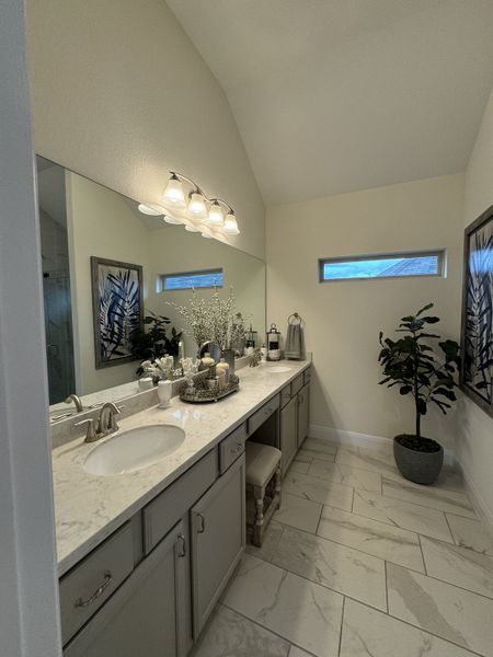 A chic bathroom with dual sinks, grey cabinetry, elegant lighting, and marble tile flooring. A chic bathroom with dual sinks, grey cabinetry, elegant lighting, and marble tile flooring.