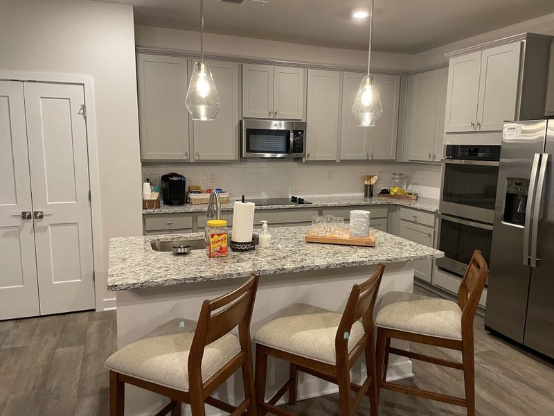 A modern kitchen with granite countertops, stainless steel appliances, and stylish pendant lighting. Wood flooring adds warmth. A modern kitchen with granite countertops, stainless steel appliances, and stylish pendant lighting. Wood flooring adds warmth.