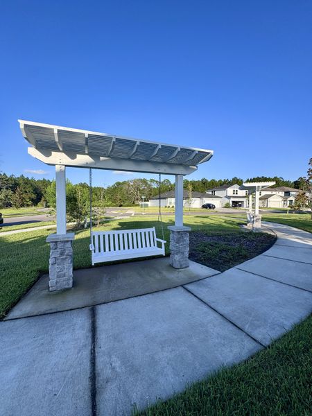 A charming white pergola with a swing in scenic Double Branch by Pulte Homes (Middleburg, FL).
