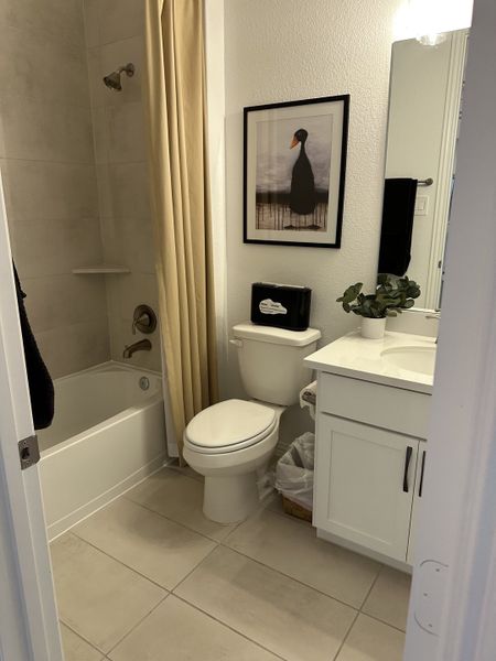 A cozy bathroom featuring a white vanity, tiled bathtub, and stylish artwork. A cozy bathroom featuring a white vanity, tiled bathtub, and stylish artwork.