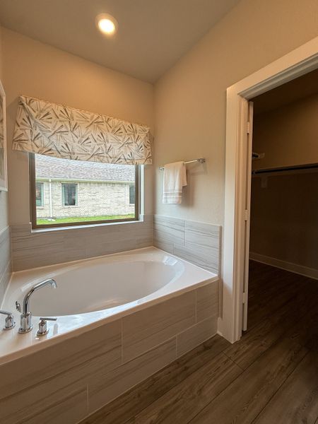 A cozy bathroom with a large tiled bathtub, natural light, and wood flooring for a relaxing atmosphere.