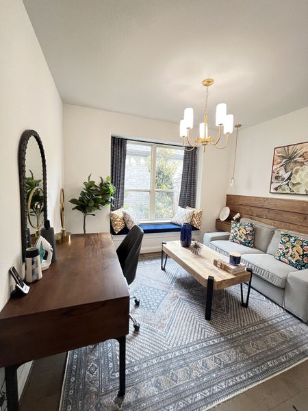 A cozy home office with a wooden desk, patterned rug, and modern chandelier.