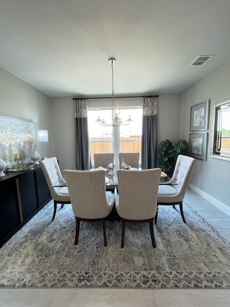 A sophisticated dining room featuring a glass table, elegant upholstered chairs, and a chic chandelier, accented by stylish decor.