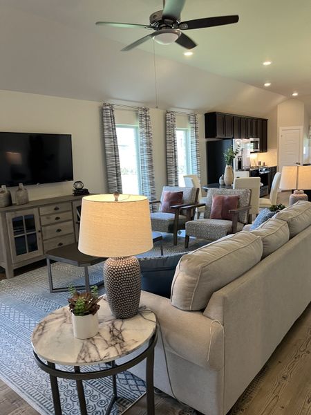 A cozy living space with a plush sofa, elegant lamps, and a view into a modern kitchen, exuding warmth and style.