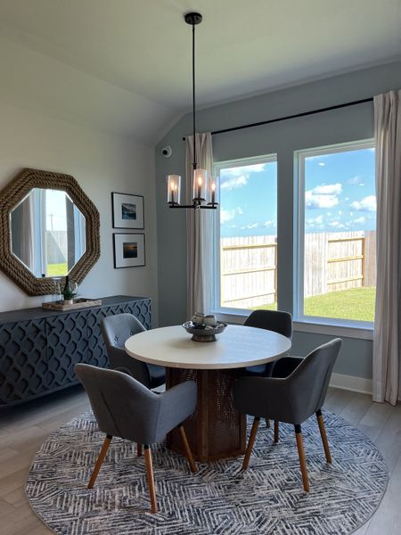 A cozy dining area with a round table, gray chairs, and a patterned rug, accented by a stylish mirror and ample natural light. A cozy dining area with a round table, gray chairs, and a patterned rug, accented by a stylish mirror and ample natural light.