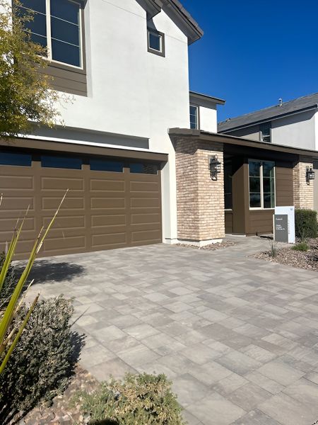 A two-story modern home with a brown garage, brick accents, and a paved driveway leading to the entrance.