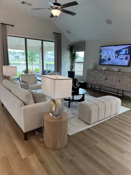 A modern living room with a cozy beige sofa, chic lighting, and large windows leading to an outdoor view.