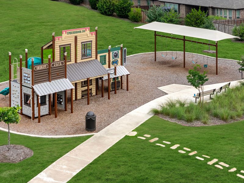 Community playground with western-themed play structure, swing set with shade canopy, and seating area on green lawn Community playground with western-themed play structure, swing set with shade canopy, and seating area on green lawn