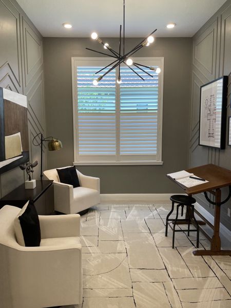 A contemporary study featuring modern lighting, geometric patterns, white chairs, and elegant decor.