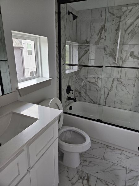 A modern bathroom with a marble-tiled shower, sleek black fixtures, and elegant white cabinetry.