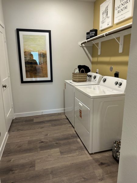 A modern laundry room featuring a washer-dryer combo, wooden flooring, and chic wall art for a stylish touch.