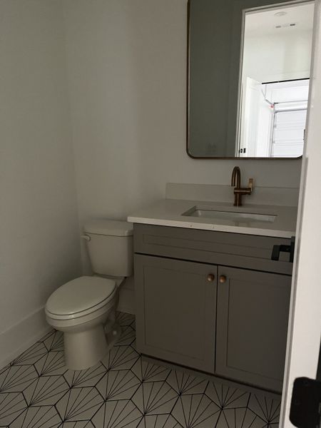 A modern bathroom featuring geometric tile flooring, a sleek vanity, and elegant gold fixtures.