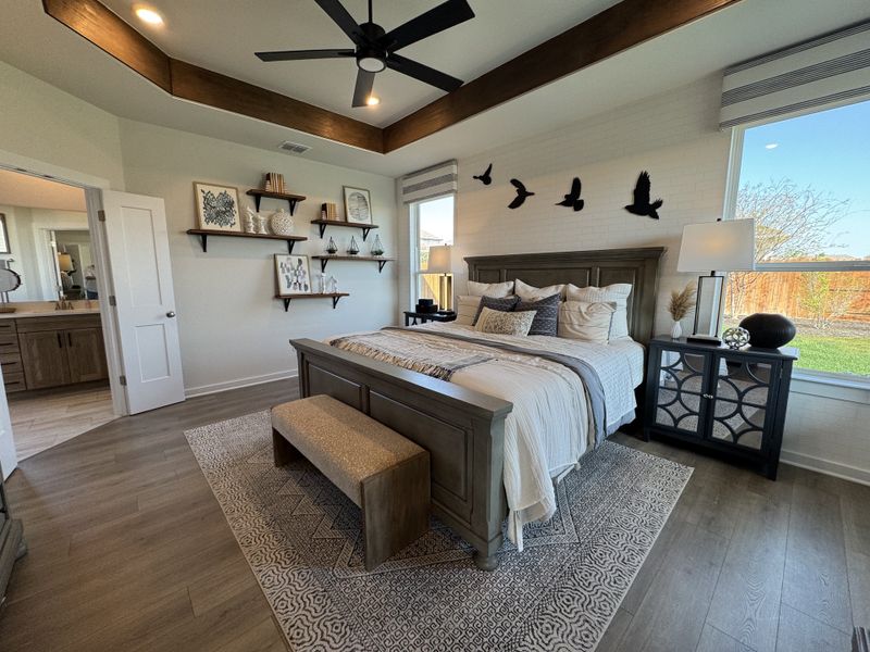 A cozy bedroom with tray ceiling, wood accents, elegant decor, and a large window offering ample natural light. A cozy bedroom with tray ceiling, wood accents, elegant decor, and a large window offering ample natural light.