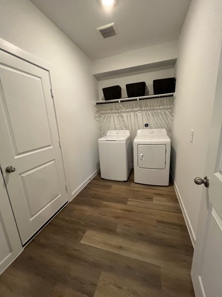 A functional laundry room with modern appliances, wood flooring, and ample shelving for organization.