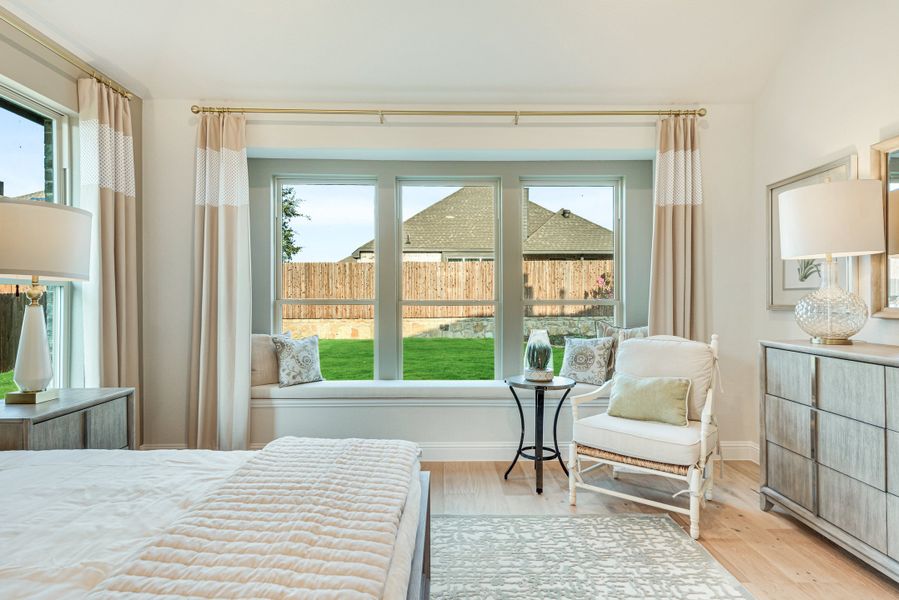 Bedroom with built-in window seat, large bay windows, hardwood floors, and white accent chair Bedroom with built-in window seat, large bay windows, hardwood floors, and white accent chair