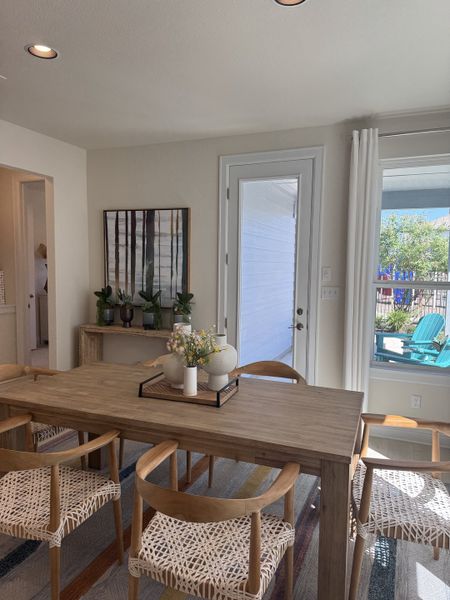 A cozy dining area with a wooden table, woven chairs, and modern decor, enhanced by natural light through large windows.