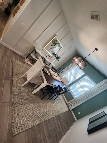 A cozy dining room with a wooden table, modern chairs, and green accent wall, enhanced by natural light and stylish decor.