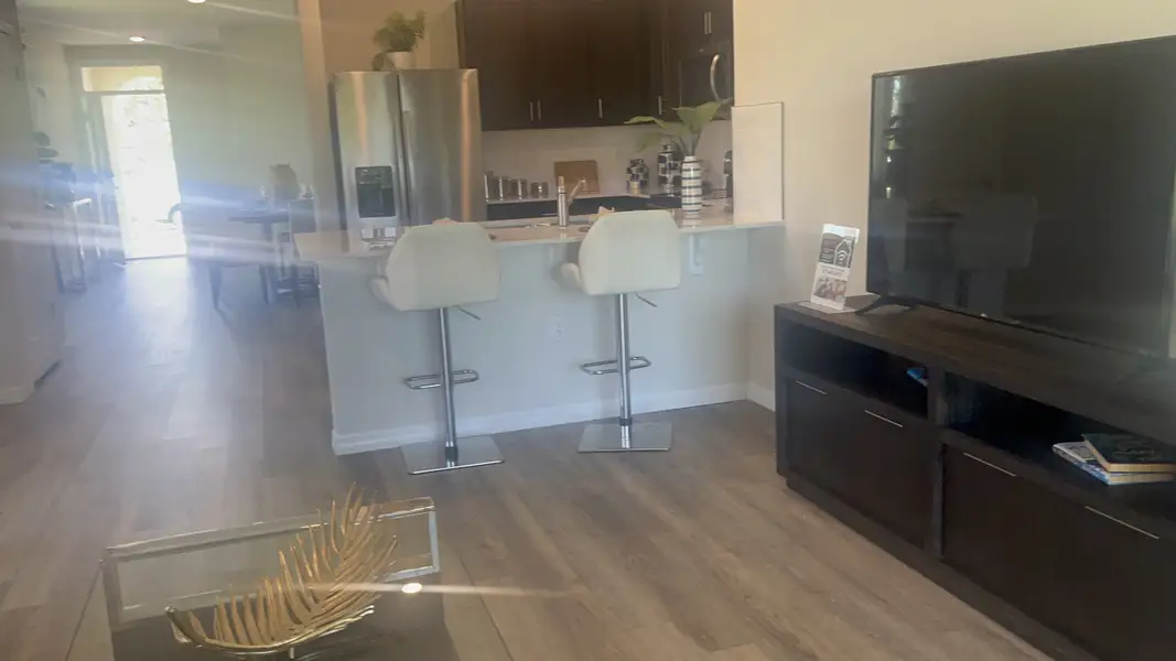 A modern open kitchen with sleek bar stools, stainless steel appliances, and warm wood flooring.