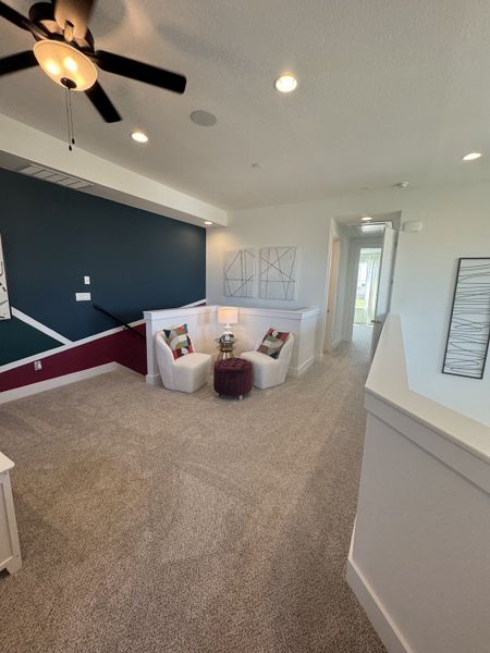 A cozy loft area with plush carpet, modern accent chairs, geometric wall art, and recessed lighting.