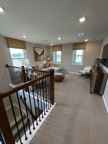 A cozy loft space with plush carpeting, a sectional sofa, abstract art, and ample natural light through large windows.
