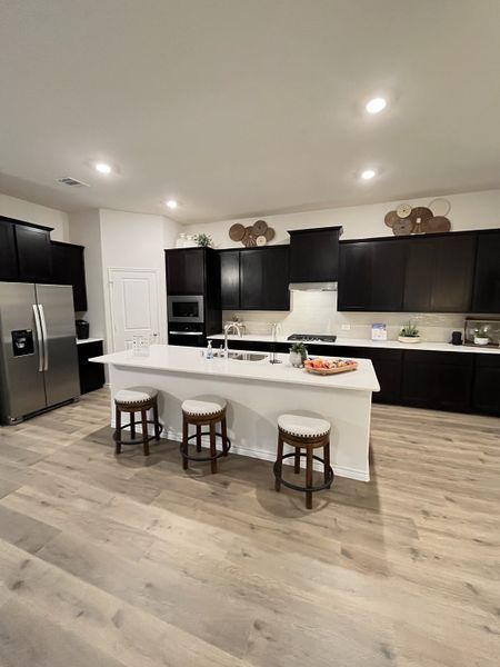 A modern kitchen with dark cabinetry, a sleek white island, and bar stools, set on elegant light wood flooring. A modern kitchen with dark cabinetry, a sleek white island, and bar stools, set on elegant light wood flooring.