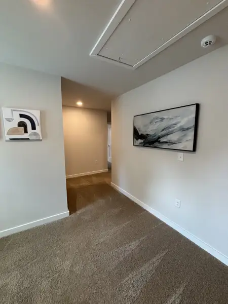 A hallway with plush carpeting, modern artwork, and recessed lighting creates a welcoming atmosphere. A hallway with plush carpeting, modern artwork, and recessed lighting creates a welcoming atmosphere.