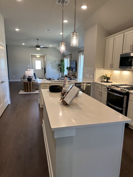 A modern kitchen with an island, sleek pendant lights, dark wood flooring, and white cabinetry, flowing into a cozy living area. A modern kitchen with an island, sleek pendant lights, dark wood flooring, and white cabinetry, flowing into a cozy living area.