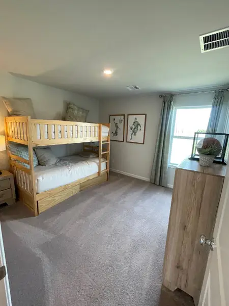 A cozy bedroom featuring a wooden bunk bed, soft carpet, and natural light through a large window with modern decor.
