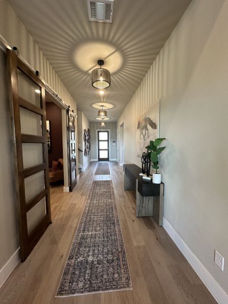 A modern hallway features elegant lighting, a long patterned runner, and sleek wood accents for a welcoming entryway. A modern hallway features elegant lighting, a long patterned runner, and sleek wood accents for a welcoming entryway.