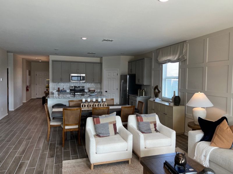 An open-plan living area with cozy seating, a modern kitchen, and stylish dining setup, featuring warm wood flooring.