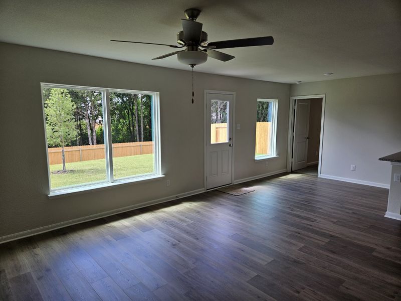 Spacious living area with wood flooring, large windows, and a ceiling fan, offering plenty of natural light and backyard views.