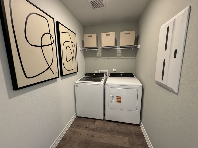 A modern laundry room with abstract art, a washer and dryer, and storage on a sleek wooden floor.