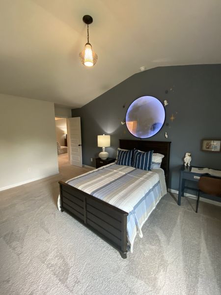 A cozy bedroom featuring a dark wooden bed, striped bedding, accent wall, and modern lighting.