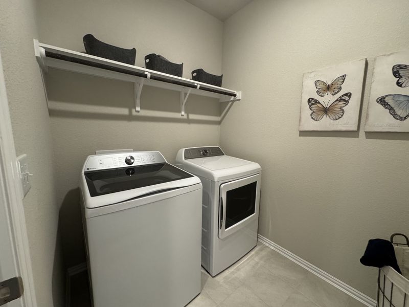 A modern laundry room with a sleek washer and dryer, wall art featuring butterflies, and practical overhead storage.