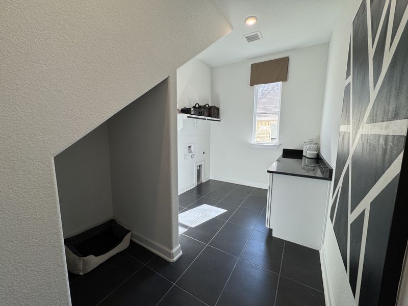 A sleek laundry room with dark tile flooring, modern cabinetry, and ample natural light.