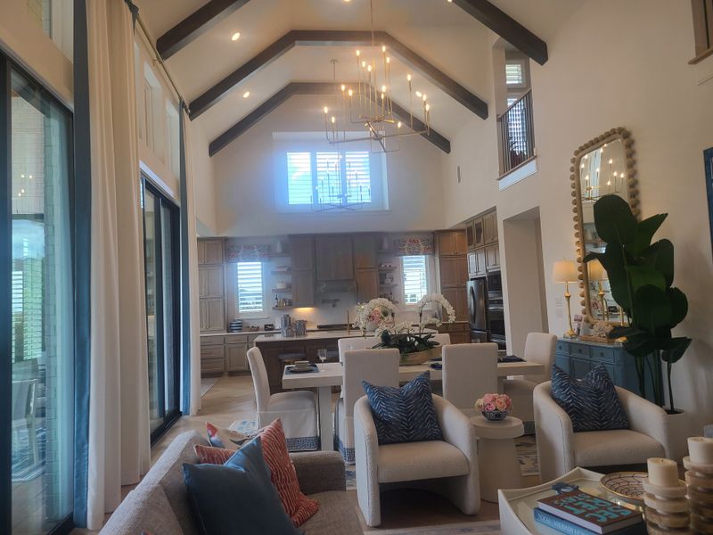 A spacious living area with vaulted ceilings, modern chandeliers, and elegant decor, leading to an open kitchen with natural light.