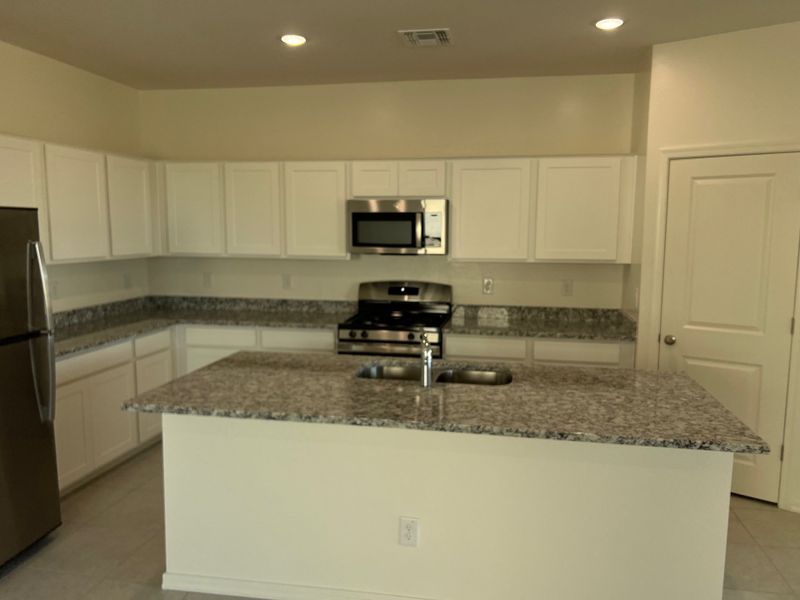 Modern kitchen featuring granite countertops, white cabinetry, and stainless steel appliances.