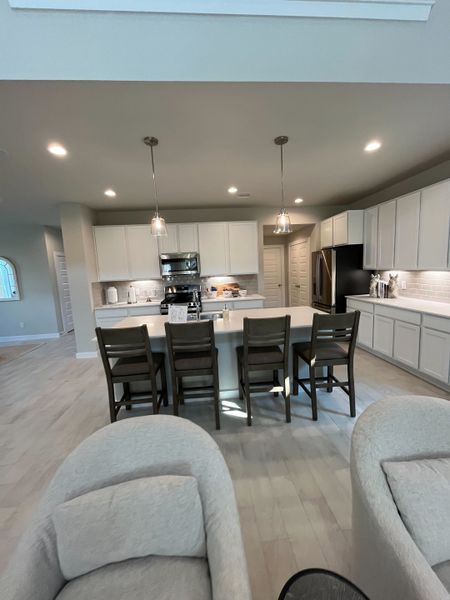 A modern kitchen with sleek white cabinetry, a large island, pendant lighting, and cozy seating arrangement. A modern kitchen with sleek white cabinetry, a large island, pendant lighting, and cozy seating arrangement.